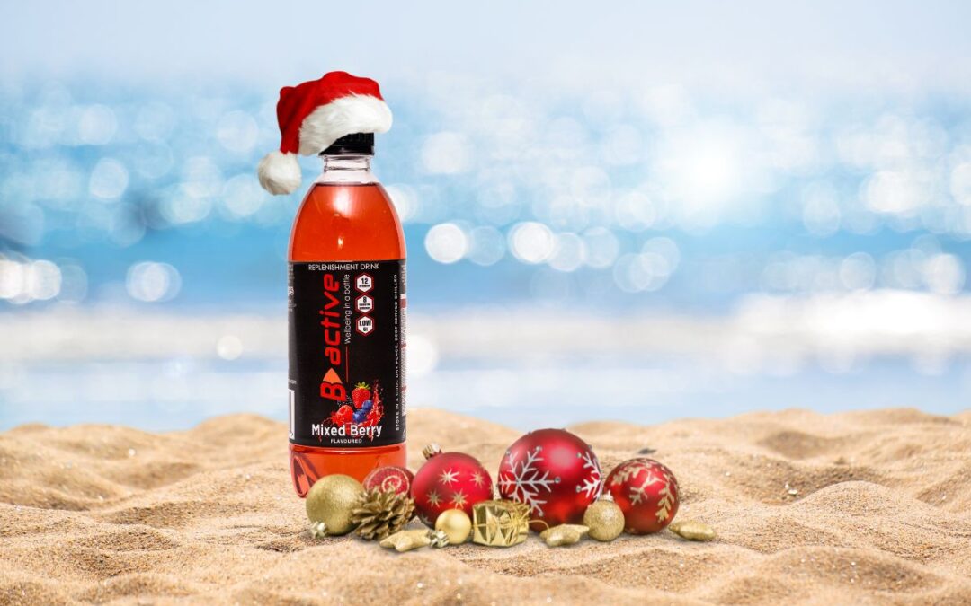 a bottle of B active on a beach with holiday baubales and a santa hat. Stay energised for the holidays!